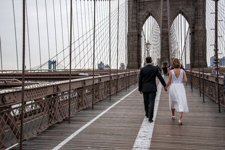 Newly married couple walking across the Brooklyn bridge (NYC) on a cloudy day
