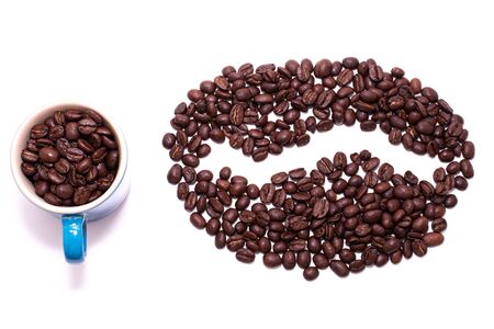 Coffee bean shape created with coffee beans and a coffee mug filled with coffee beans over a white backgroundの写真素材