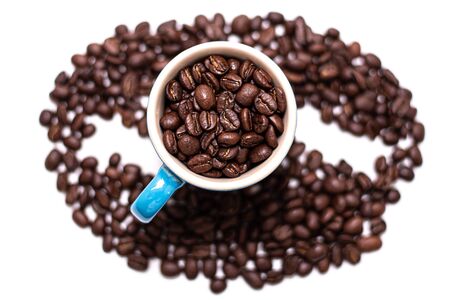 Coffee bean shape created with coffee beans and a coffee mug filled with coffee beans over a white backgroundの写真素材