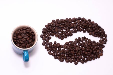 Coffee bean shape created with coffee beans and a coffee mug filled with coffee beans over a white backgroundの写真素材