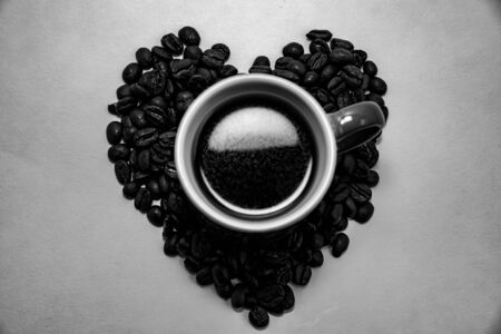 Heart shape created with coffee beans and a coffee mug filled with coffee beans over a white backgroundの写真素材