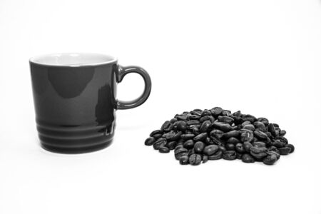 Black and white porcelain cup filled with coffee close to a group of coffee beansの写真素材
