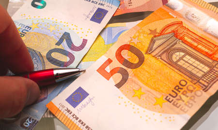 Euro banknotes and a man's hand with a pen close-upの写真素材