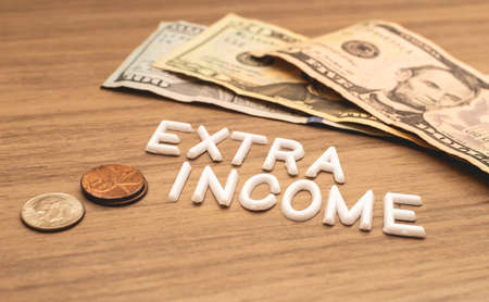 The word EXTRA INCOME is written in white letters on a wooden background next to money.の写真素材