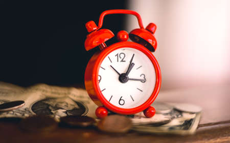 Time is money. Red alarm clock with money on wooden table.の写真素材