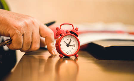 Close up of man hand holding red alarm clock with notebook and pen on wooden table.の写真素材