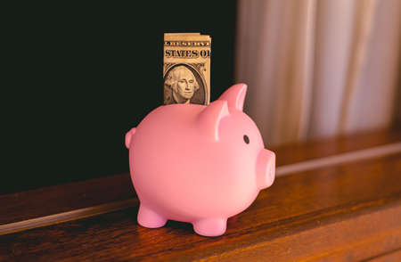 Pink piggy bank with dollar banknote on the wooden table.の写真素材