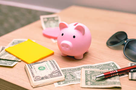 Piggy bank, money, pen and glasses on wooden tableの写真素材