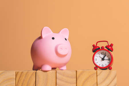 Pink piggy bank with alarm clock on wooden blocks. Time is money concept.の写真素材