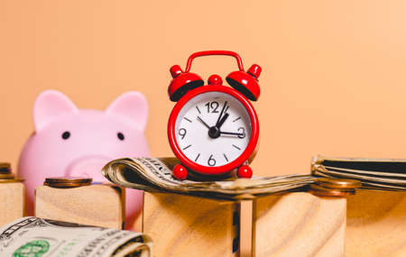 Alarm clock and piggy bank with dollar banknotes on wooden backgroundの写真素材