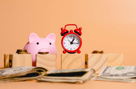 Piggy bank and alarm clock with dollar banknotes on a beige background.の写真素材