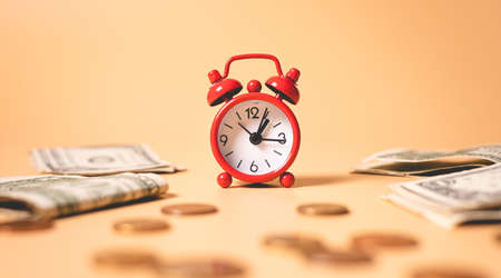 Time is money. Red alarm clock and dollars on a yellow background.の写真素材