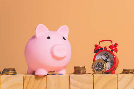 Pink piggy bank with coins and alarm clock on wooden background.の写真素材