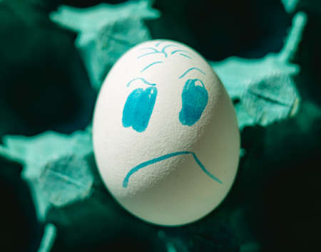 Angry face chicken white egg on a tray. Close-up photo. Concept of emotions and life difficulties.