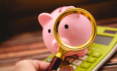 Piggy bank with magnifying glass and coins on wooden backgroundの写真素材