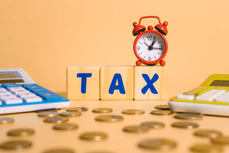 The word TAX is written on wooden cubes next to a red alarm clock and a calculator.