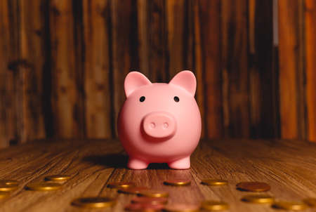 Pink piggy bank with coins on wooden background. Saving money concept.の写真素材