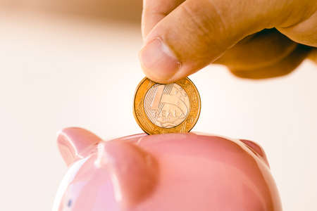 Hand putting a coin into a pink piggy bank on a white background