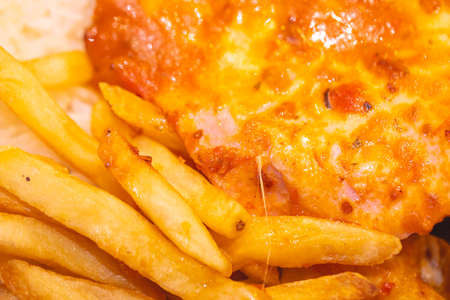 Close up of fried chicken fillet with cheese and french fries.