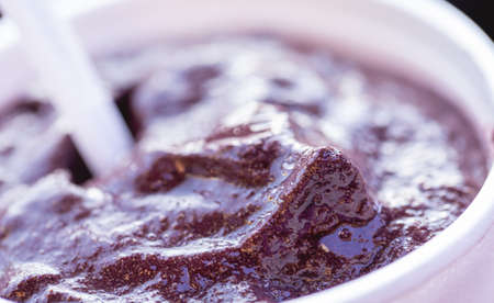 Homemade chocolate ice cream in a white cup on a black background.