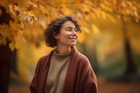 Portrait of a smiling young woman standing in autumn park and looking awayの素材