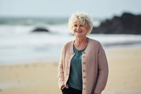 Portrait of smiling senior woman standing on beach with ocean in backgroundの素材