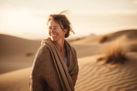 Portrait of happy mature woman wrapped in blanket standing in desert and looking awayの素材