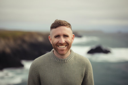 Portrait of handsome man smiling at camera while standing by the oceanの素材