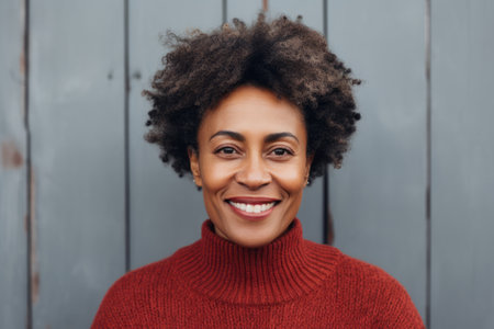 Portrait of a smiling young african american woman in red sweater standing against wooden backgroundの素材
