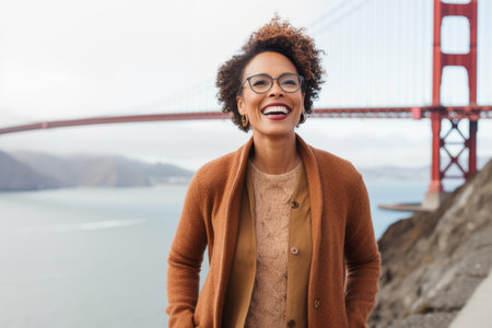 Portrait of a smiling young woman with afro hairstyle wearing coat and eyeglasses standing with hand in pocket and looking at cameraの素材