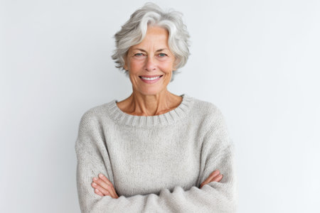 Portrait of a happy senior woman standing with arms crossed over white backgroundの素材