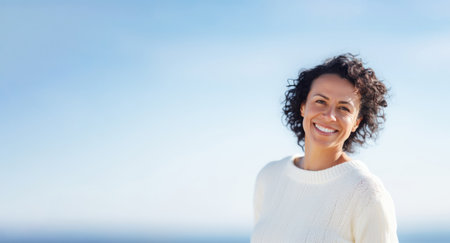 smiling young woman in white sweater on the beach over blue skyの素材
