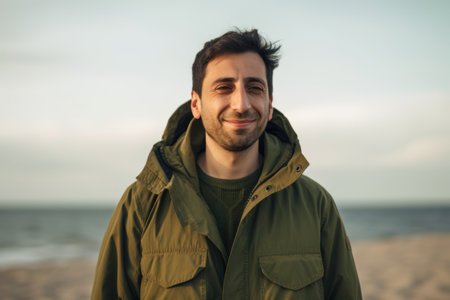 Portrait of handsome young man in green jacket standing on beach.の素材
