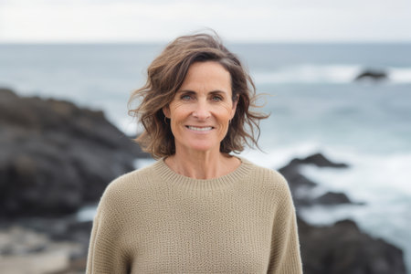 Portrait of smiling mature woman standing at the beach with ocean in backgroundの素材