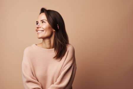 Portrait of a smiling young woman looking away isolated over beige backgroundの素材
