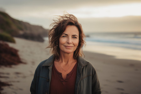Portrait of a beautiful mature woman standing on the beach at sunsetの素材