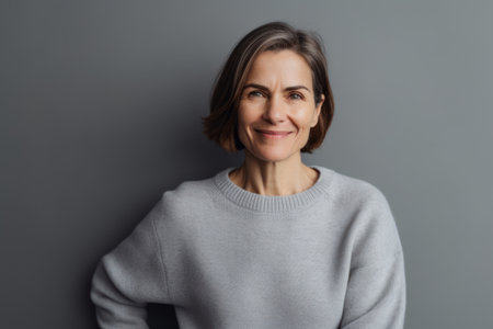 Portrait of smiling mature woman in gray sweater looking at camera isolated on gray backgroundの素材