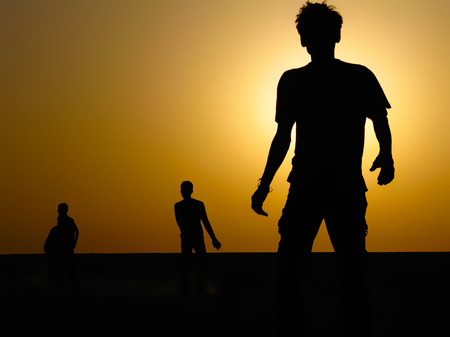 Silhouette of Boys Playing on a Field Against Warm Sunrise Skyの写真素材