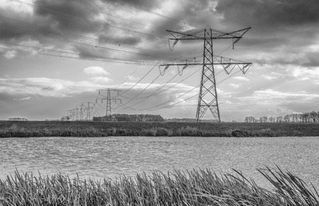 Black and white photograph of a landscape with a long row of power pylons. Threatening clouds are visible above the land.の写真素材
