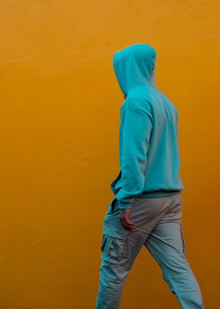 Hooded boy walking on yellow wallの写真素材