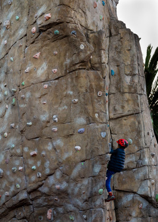 A boy climbing on a rock climber with a red helmetの写真素材