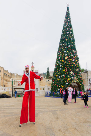 NAZARETH, ISRAEL - December 19, 2014: Santa Claus figure on stilts, local and visitors, and a Christmas tree, in the square of the Greek Orthodox Church of Annunciation, in Nazareth, Israelのeditorial素材