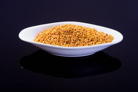 Fenugreek seeds in a white bowl on black surfaceの写真素材