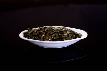 Pumpkin Seeds in a white plate on a black backgroundの写真素材