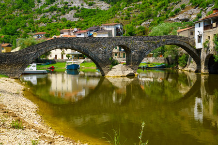 RIJEKA CRNOJEVICA, MONTENEGRO - JUNE 30, 2015: The Rijeka Crnojevica Bridge and village, with locals and tourists, in Rijeka Crnojevica, Montenegroのeditorial素材