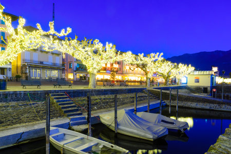ASCONA, SWITZERLAND - DECEMBER 28, 2015: Sunset scene of the lake promenade Piazza Mota, with Christmas decoration, locals and visitors, in Ascona, Ticino, Switzerlandのeditorial素材