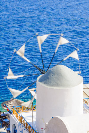 THIRASIA, GREECE - SEPTEMBER 29, 2011: Aegean Sea coast scene with restaurant, windmill, volcanic cliff, locals and visitors, in Thirasia, Santorini, Greeceのeditorial素材