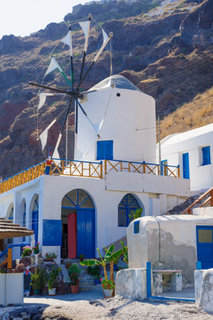 Aegean Sea coast scene with restaurant, windmill, volcanic cliff, in Thirasia, Santorini, Greeceのeditorial素材