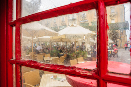 VALLETTA, MALTA - APRIL 13, 2012: Scene of a square with restaurants, locals and visitors, as viewed from a typical phone booth, in Valletta, Maltaのeditorial素材