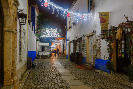 OBIDOS, PORTUGAL - DECEMBER 27, 2017: View of an alley in the old town, with local businesses, Christmas decorations, locals and visitors, in Obidos, Portugalのeditorial素材